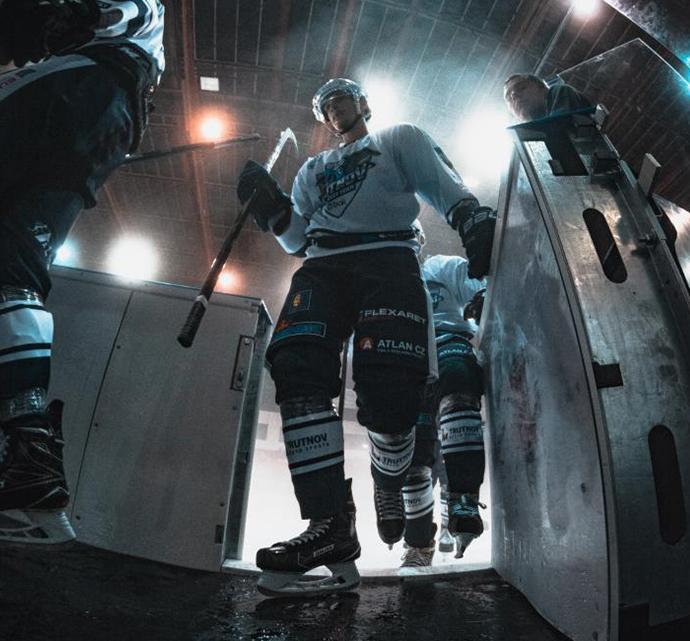 Hockey players entering an arena, lit dramatically from above, for a night game.