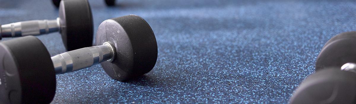 Close-up of a barbell on speckled textured blue and black rubber gym flooring.