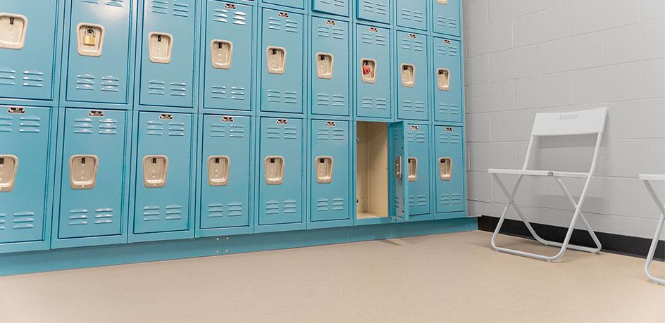 Interior of a locker room with rows of blue lockers and a white folding chair.