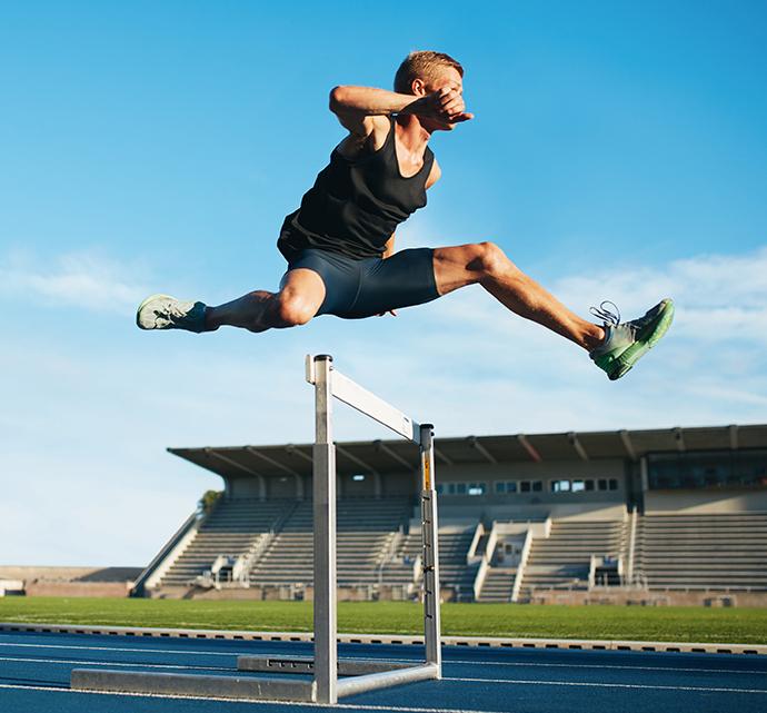 Male athlete hurdling over a track barrier in a stadium during a training session.