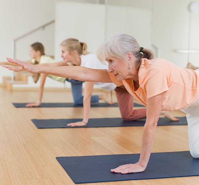 Senior woman participating in a yoga class with others in a fitness studio.