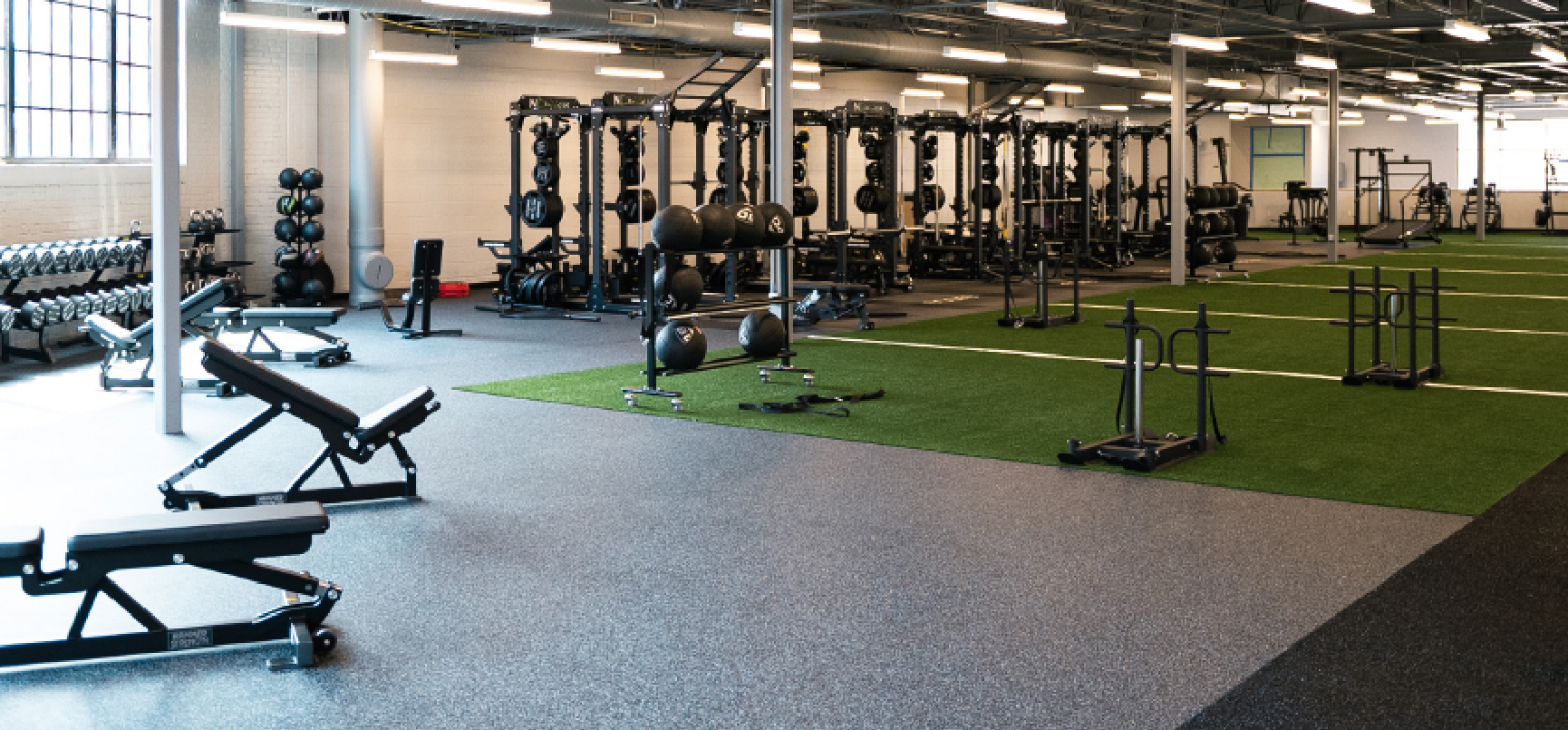 Large, well-equipped gym with varied strength training equipment and a green artificial turf area.