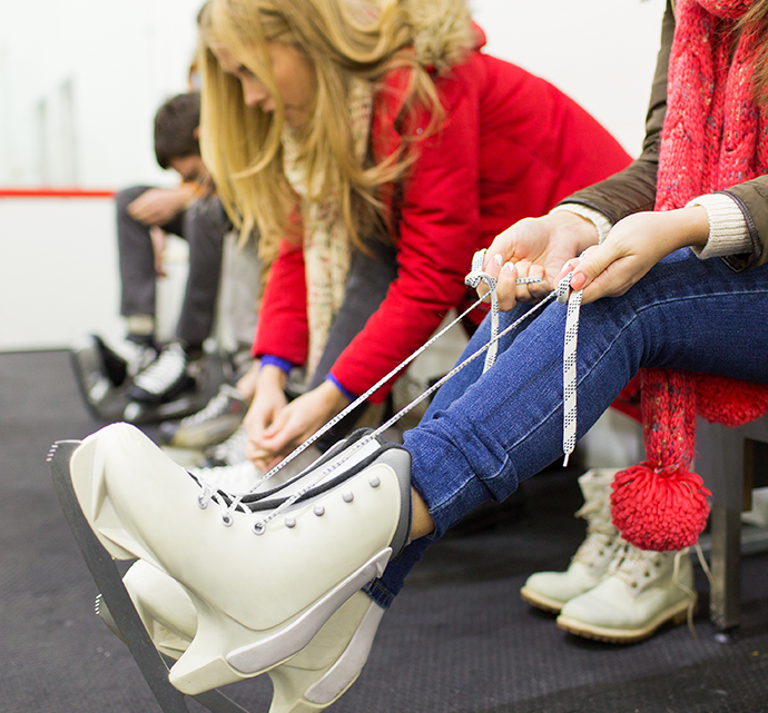 People tying their ice skates on a bench in an indoor skating rink area.